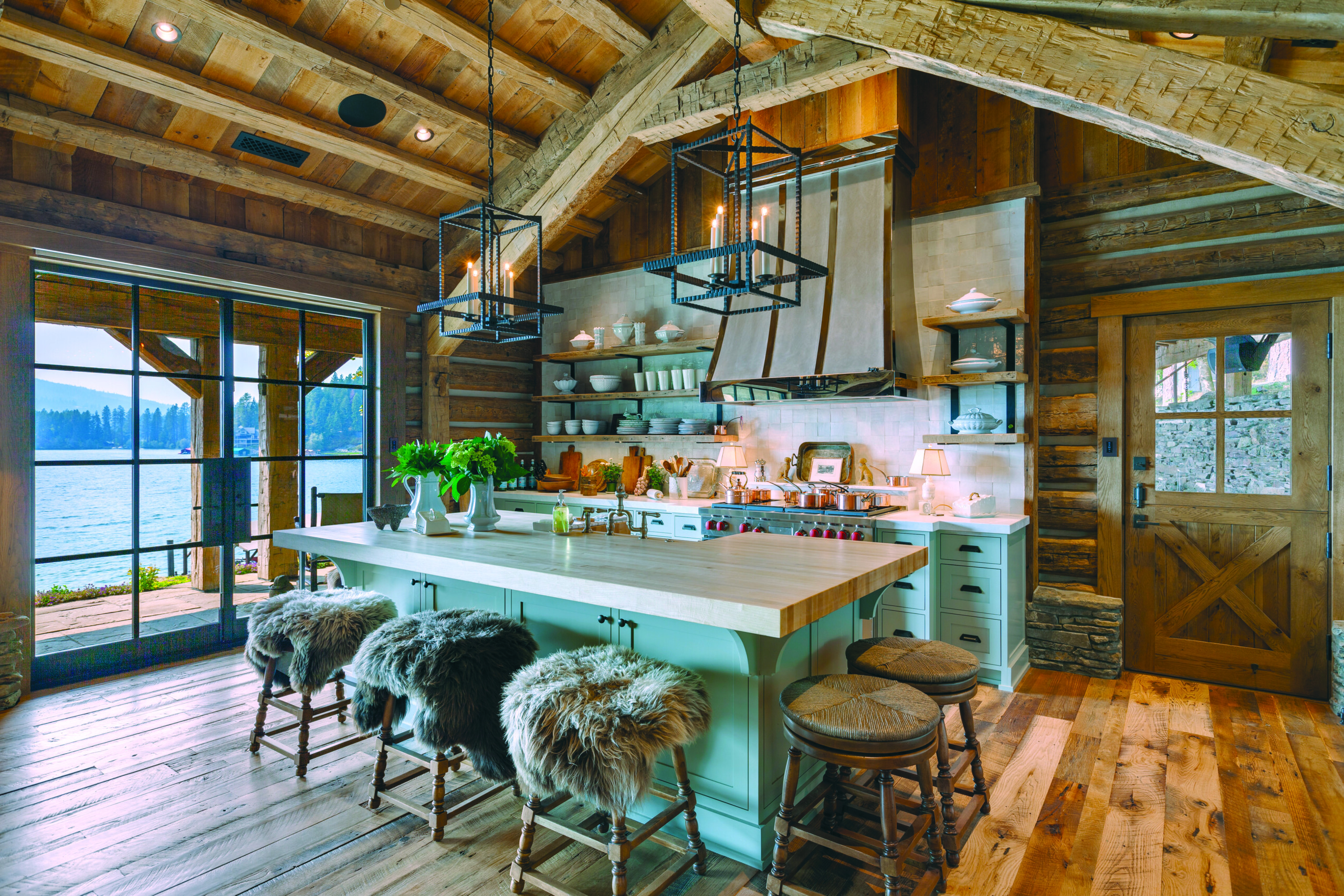 The open kitchen in the main cabin features the homeowners’ finds from sustainable shopping site Chairish, including Paul Ferrante pendant lighting, as well as new woven-top counter stools from Chaddock. Floor and ceiling beams are reclaimed oak and Douglas fir. | Photo: Mike McCall
