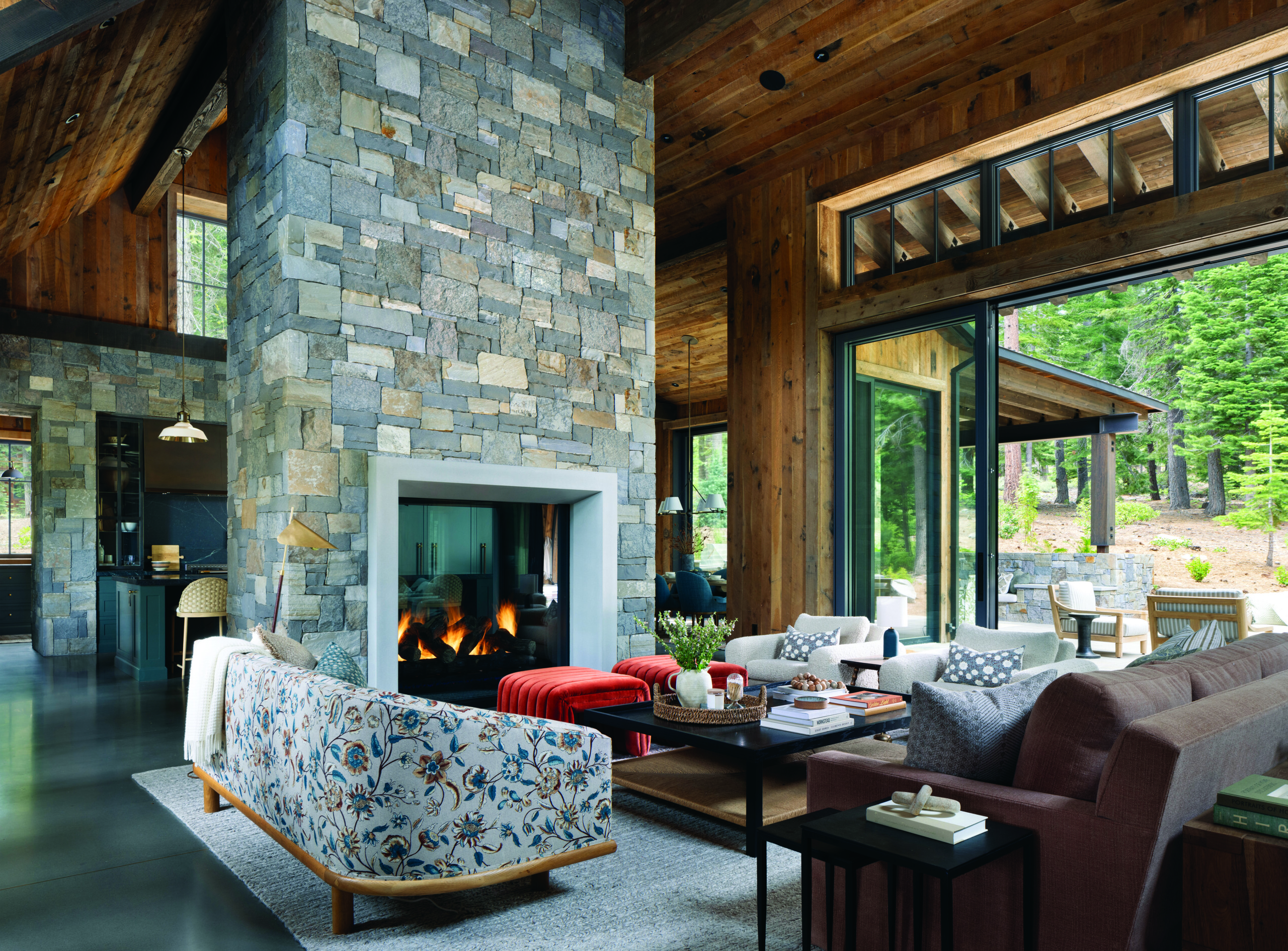 The floral print fabric on the Nickey Kehoe sofa and the bouclé chairs by Lawson-Fenning provide soft counterpoints to the stacked-stone fireplace. The custom ottomans wear JAB Velluto, and the coffee table is from Shoppe Amber Interiors. | Paul Dyer